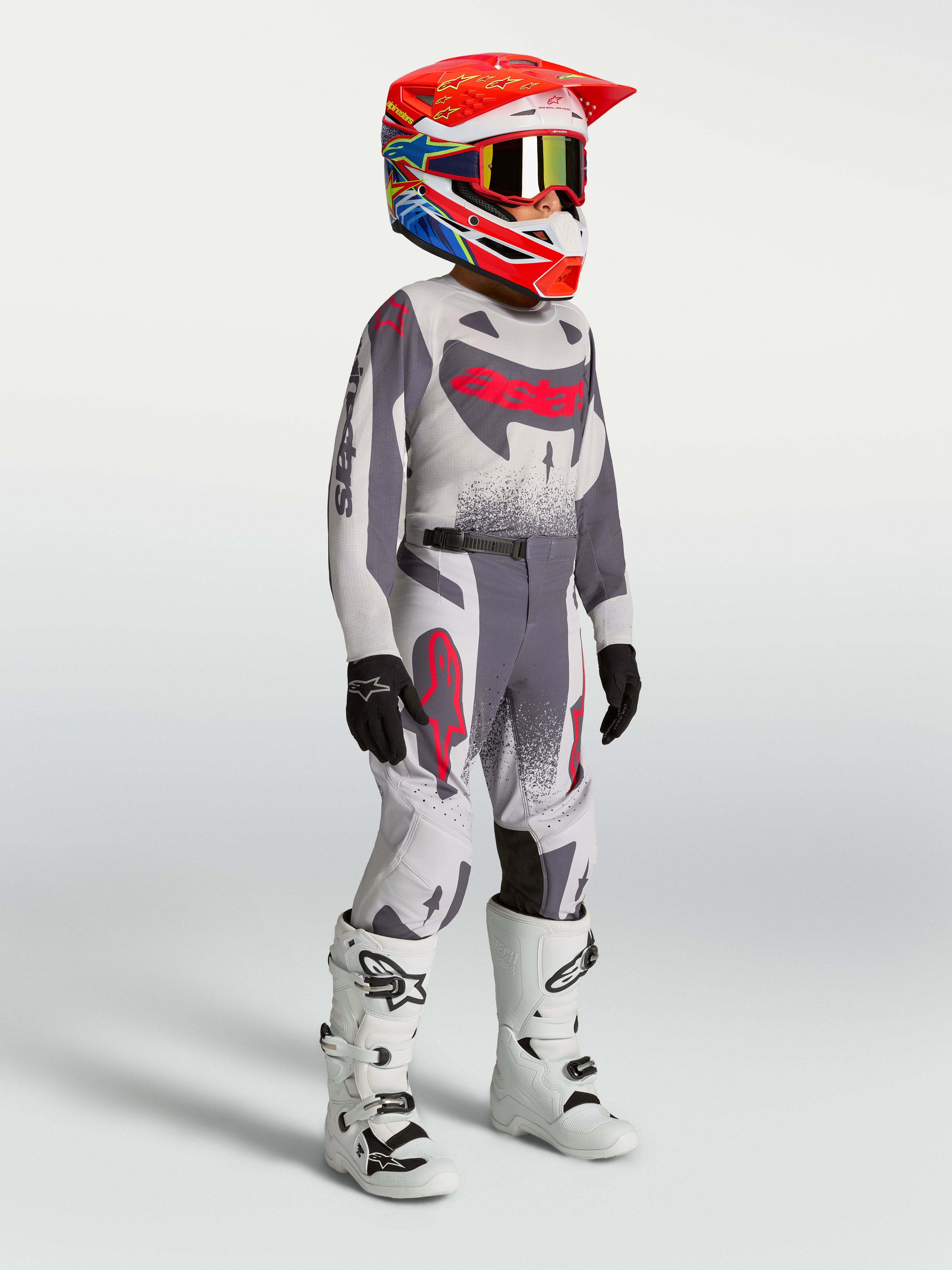 Alpinestars ungdom Supertech Swan motocross-set, grå och röd fluo tröja och byxor med vita motorcykelstövlar.