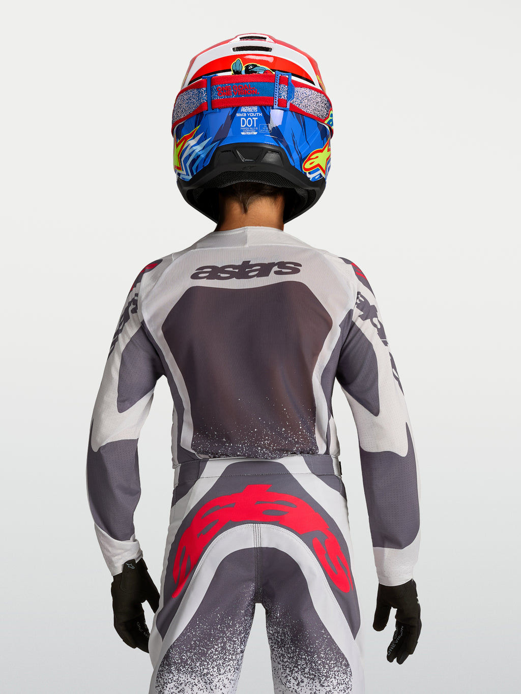 Alpinestars Ungdom Supertech Swan motocrosströja och byxor, grå och vit med röd fluo, vy bakifrån på modell.