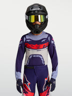 Alpinestars 2027 Supertech Dyna ungdomströja, lila och grå motocrosströja med röd logotyp, atletisk tävlingspassform i stretchmesh för terrängkörning, bärs med matchande byxor och hjälm.