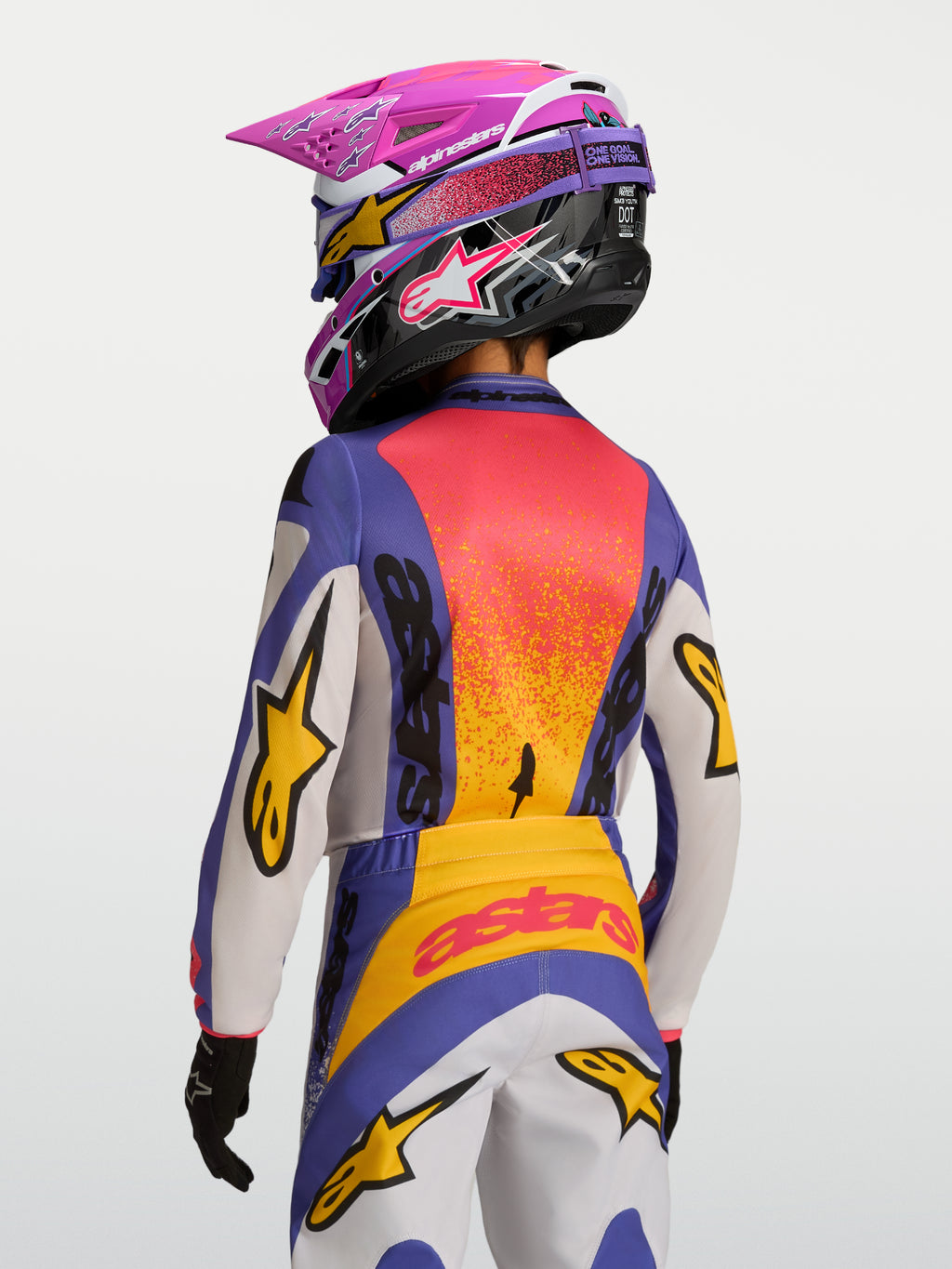 Alpinestars 2027 Ungdom Fluid Drag tröja, lila och orange motocrossracingtröja, fukttransporterande polytyg, visas bakifrån på en förare med matchande hjälm och byxor för terrängkörning.