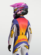 Alpinestars 2027 Ungdom Fluid Drag tröja, lila och orange motocrossracingtröja, fukttransporterande polytyg, visas bakifrån på en förare med matchande hjälm och byxor för terrängkörning.