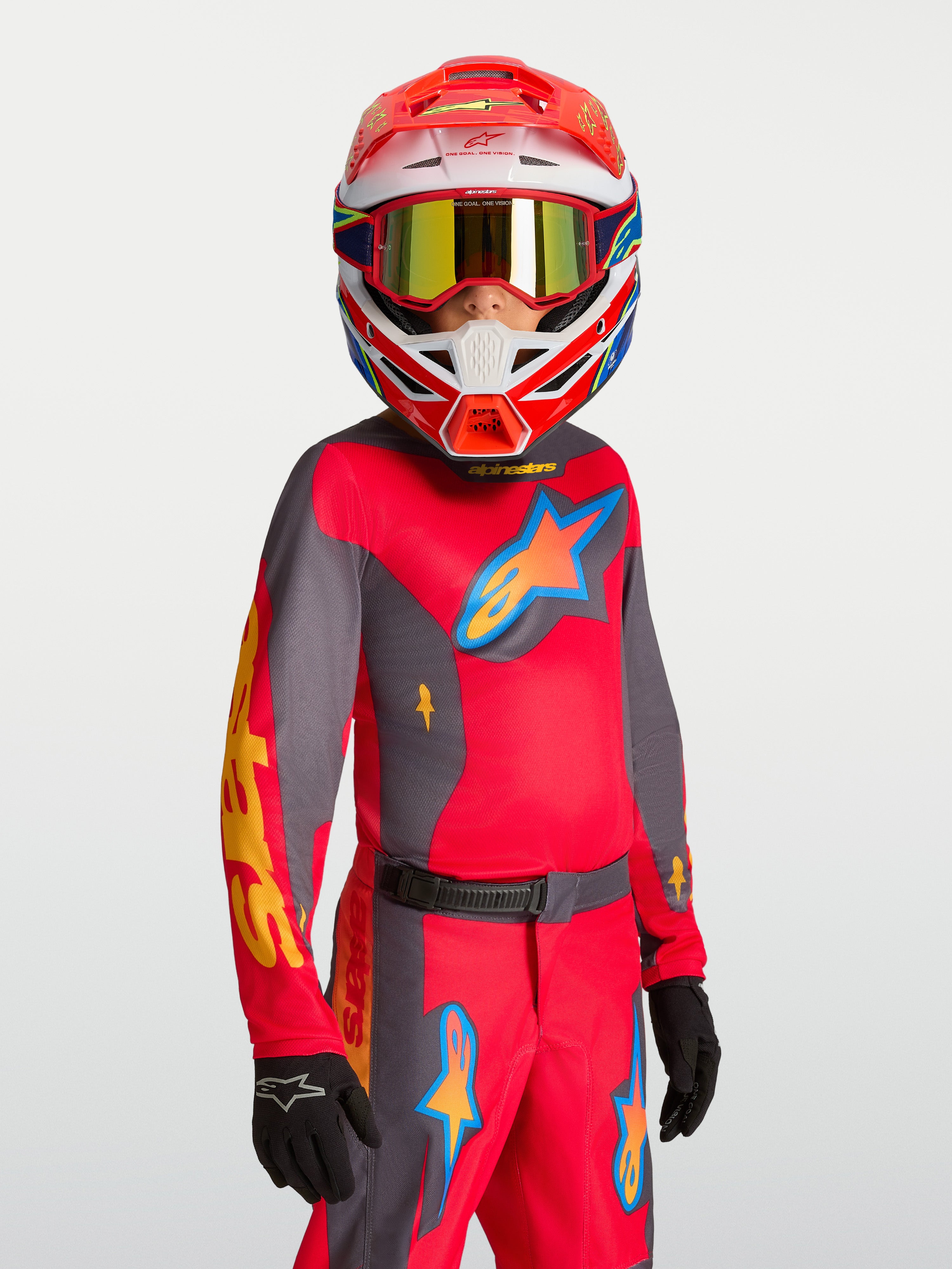 Alpinestars 2027 Fluid Hunt ungdomströja, röd och grå motocrosströja för ungdomar, fukttransporterande polytyg, bärs av modell med matchande hjälm och handskar för terrängkörning.