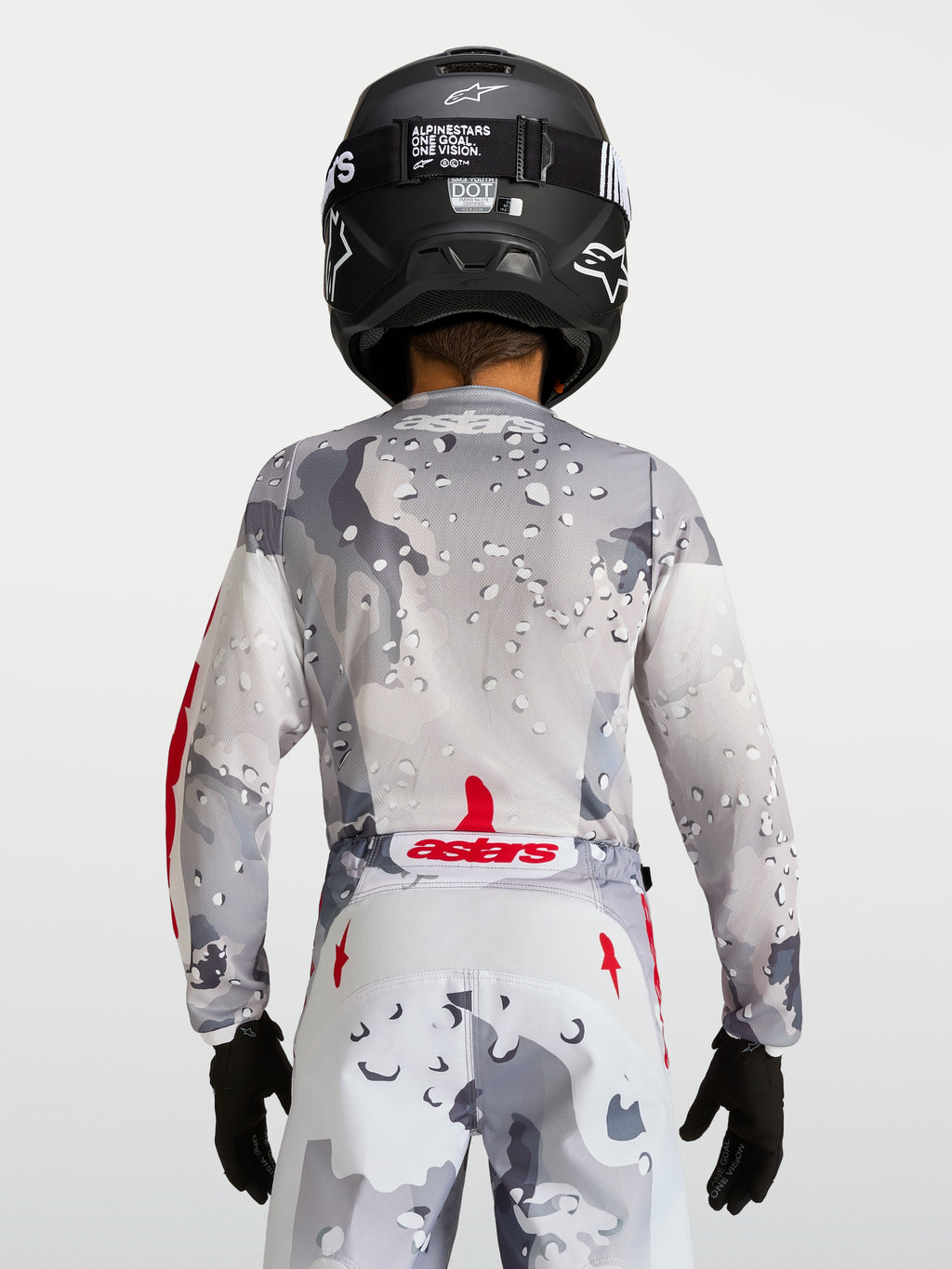 Alpinestars 2027 ungdom Fluid Lone tröja, grå kamouflagemönstrad motocrosströja, vy bakifrån, röda detaljer, svart hjälm.
