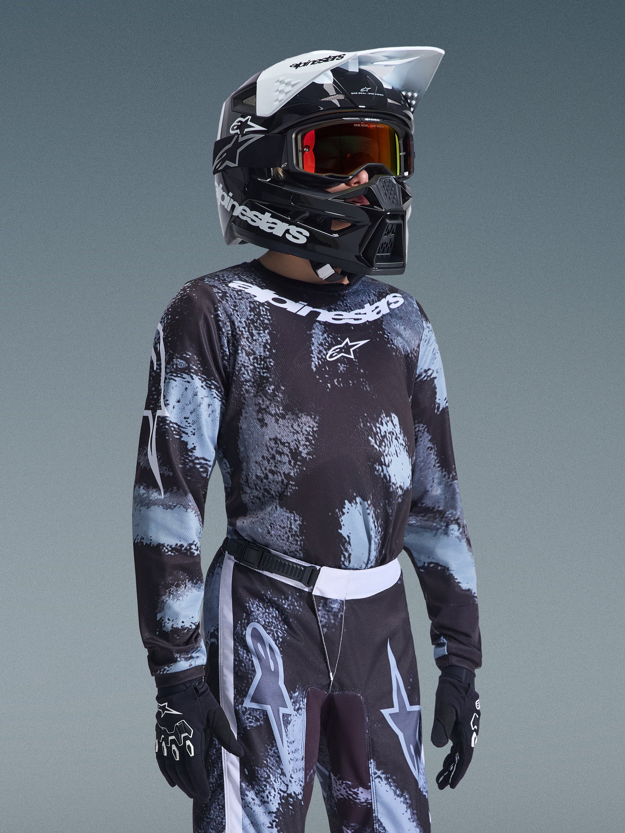 Alpinestars 2026 Ungdom Fluid Lahnd-tröja, motocrosströja, Iron Camo-mönster i svart och ljusblått, buren av en ung förare med matchande byxor och svart hjälm, koordinerad racingutrustning för terrängkörning.