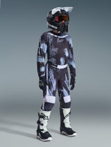 Ungdomsförare i motocross som bär 2026 Youth Fluid Lahnd-tröja i Iron Camo, svart och grått kamouflagemönster, matchande byxor, svart Alpinestars-hjälm med goggles, svarta och vita stövlar och svarta handskar, komplett motocrossutrustning för ungdomar