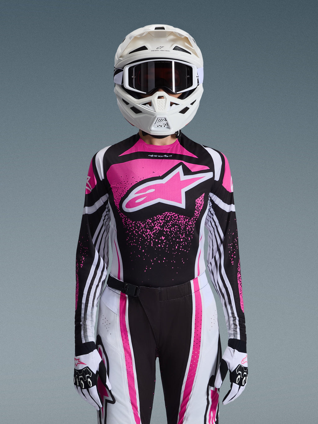 Alpinestars 2026 Stella Techstar Nomur utrustningsset, motocrossoutfit för dam, rosa, svart och vit med stor stjärnlogotyp, innehållande matchande tröja, byxor och handskar med en vit hjälm, sedd framifrån på grå bakgrund