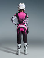 Alpinestars 2026 Stella Techstar Nomur-utrustningsset, kvinnlig motocrossförare sedd bakifrån, rosa och svart tröja med vitrandiga ärmar och spräckligt mönster, matchande byxor med vit Alpinestars-logotyp, vit hjälm och vita offroad-stövlar