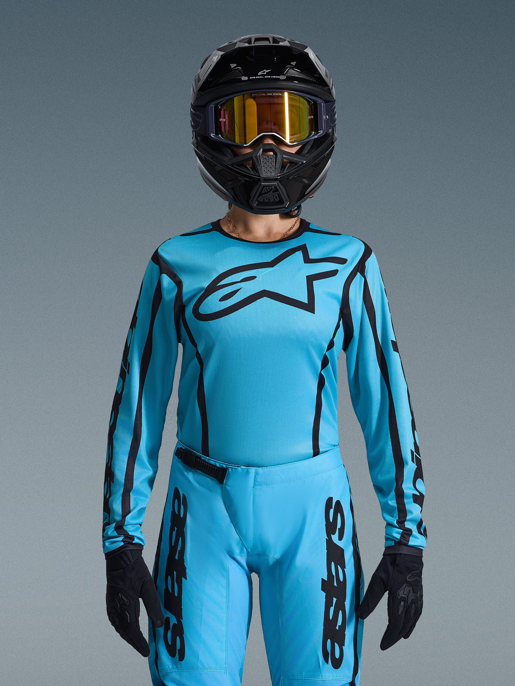 Alpinestars 2026 Stella Fluid Apex utrustningsset för dam, ljusblå tröja med svarta konturer och logotyp, matchande byxor, svart hjälm med iriserande guldfärgade goggles och svarta handskar, koordinerad motocross-racingoutfit för damer
