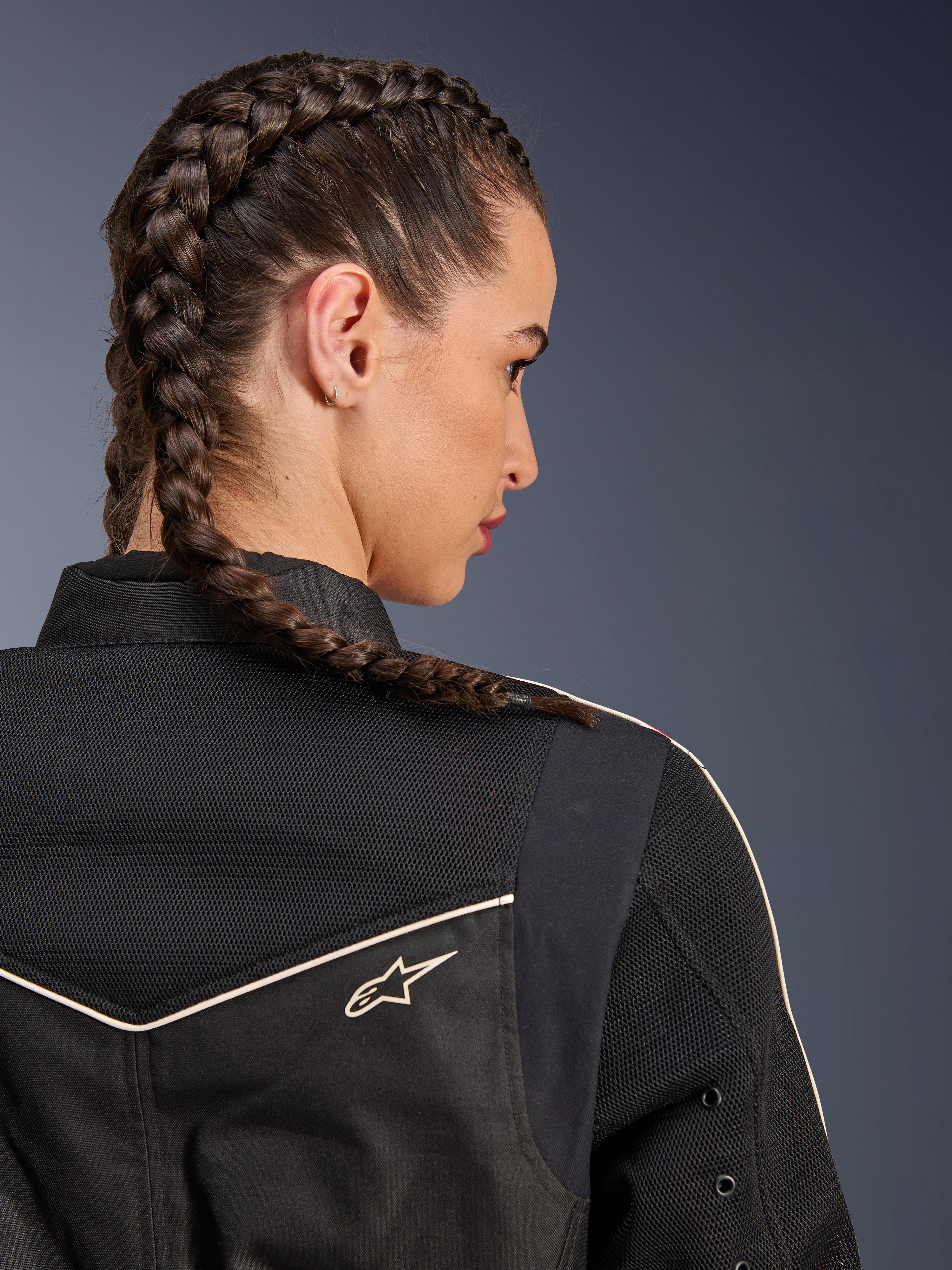 Woman wearing the Alpinestars Stella T-Dyno Air Jacket, close-up rear view focusing on the shoulders and yoke, Black with breathable 3D mesh panels, white piping and small Astars logo, model with braided hair, urban motorcycle riding apparel