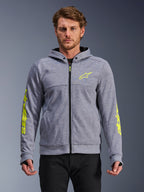 Alpinestars Chrome V2 Sport Hoodie, gråmelerad och neongul, sedd framifrån på modell, motorcykelhoodie i teknisk fleece med dragkedja framtill, neongul stjärnlogotyp på bröstet och logotyper på ärmarna, avslappnad urban körutrustning