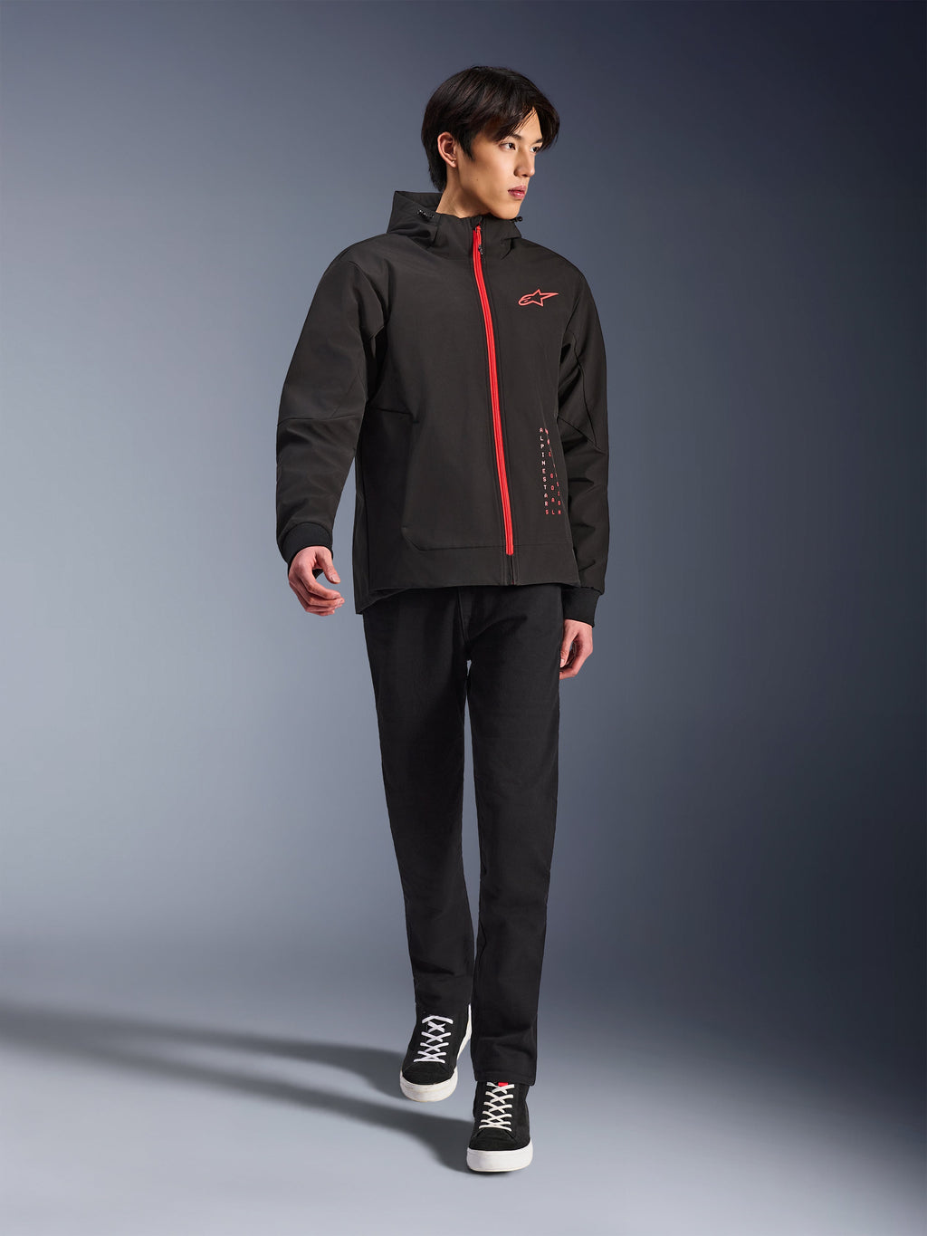 Alpinestars Radium Tech Hoodie in Black Bright Red, urban motorcycle jacket worn by a model, featuring a red front zipper and chest logo, styled with black pants and sneakers for a modern commuting look.
