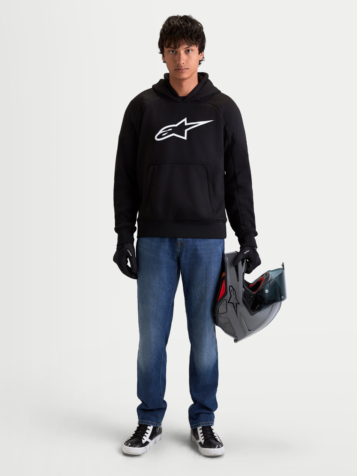 Alpinestars Ageless Hoodie, men's urban motorcycle hoodie in black with a prominent white Astar logo on the chest, worn by a model holding a helmet and wearing riding gloves, casual CE certified protective motorcycle apparel.