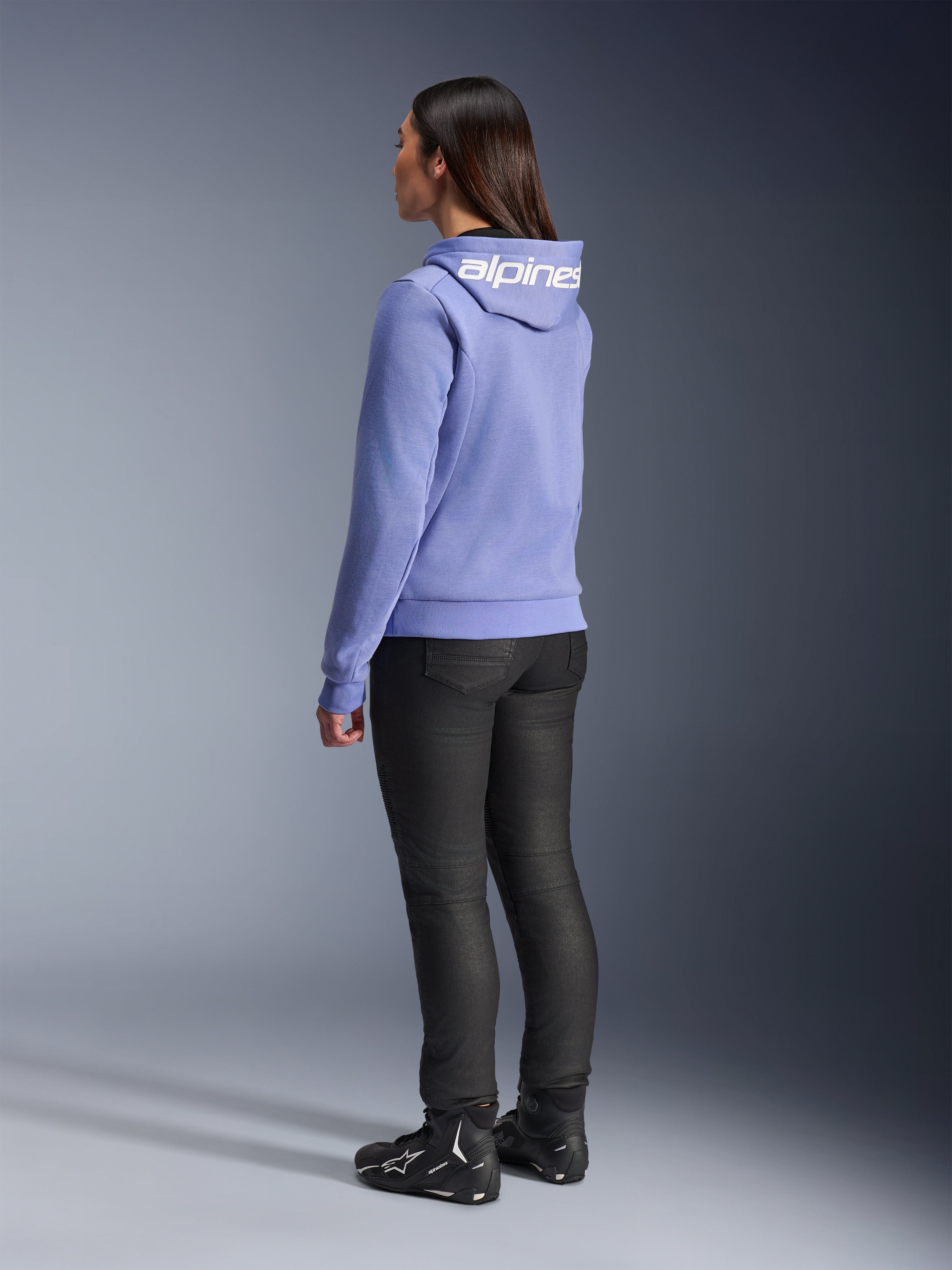 Alpinestars Stella Chrome V2 Sport Hoodie för damer, blålila, vy bakifrån som visar vit logotyp på huvan, bärs med svarta mc-byxor och svarta motorcykelstövlar, avslappnad urban motorcykelutrustning