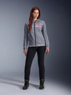 Alpinestars Stella Chrome V2 Sport Hoodie, gråmelerad och fluorescerande rosa, bärs av en kvinna med svarta byxor och stövlar, med en rosa Alpinestars-stjärnlogotyp på bröstet, urban motorcykelutrustning med hel dragkedja, lätt teknisk fleece med en avslappnad atletisk passform.