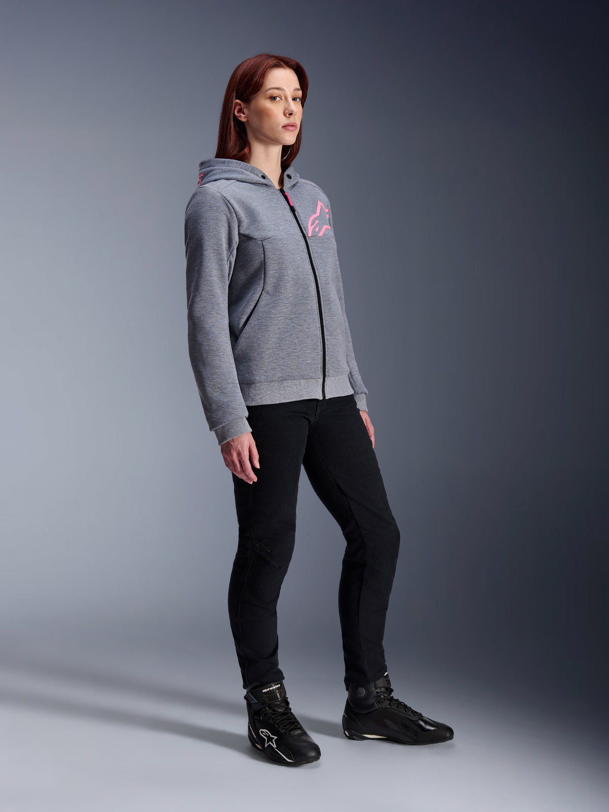 Alpinestars Stella Chrome V2 Sport Hoodie, motorcykeltröja för dam, gråmelerad och neonrosa, bärs med svarta körbyxor och svarta stövlar, avslappnad urban mc-utrustning