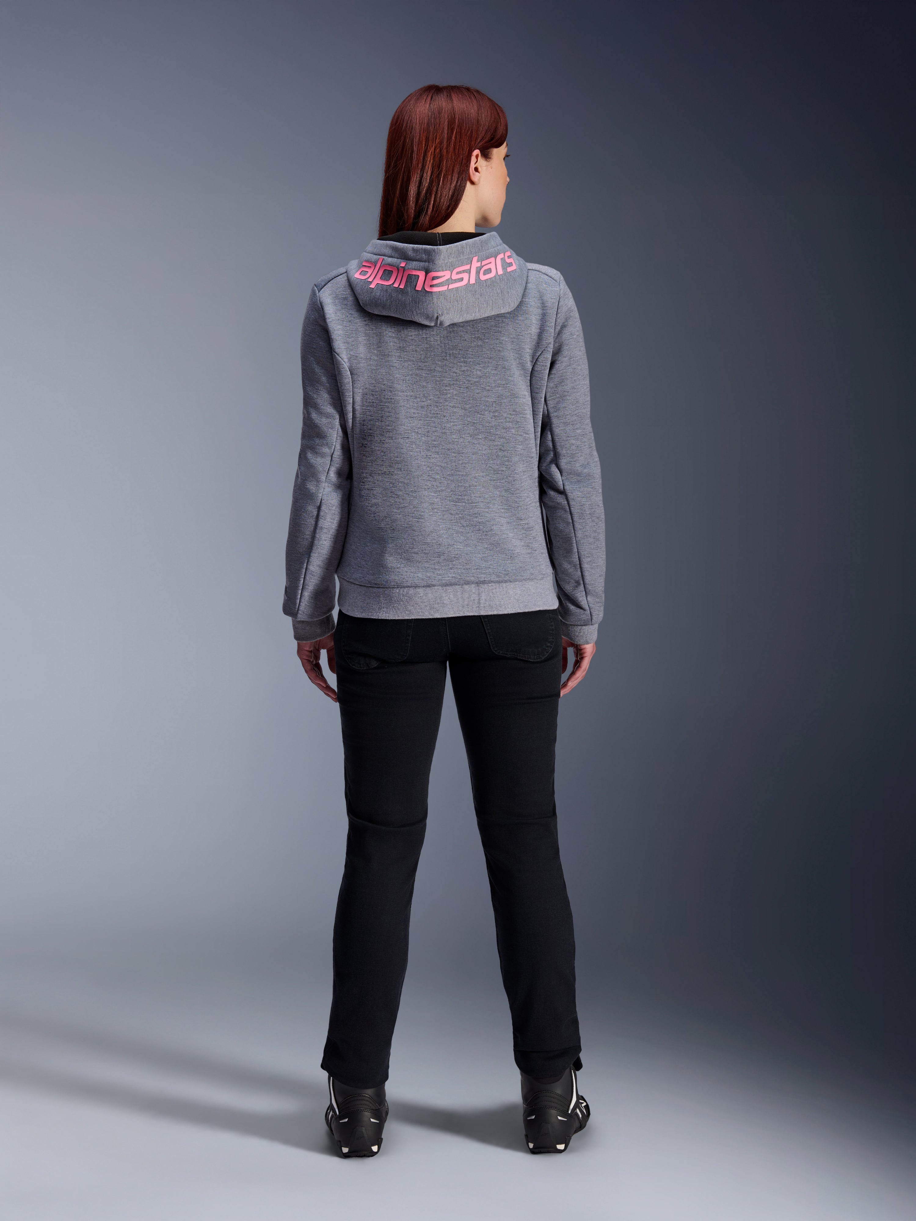 Alpinestars Stella Chrome V2 Sport Hoodie, motorcykelhoodie för dam, gråmelerad och fluorescerande rosa, vy bakifrån som visar rosa Alpinestars-logotyp på huvan, bärs med svarta mc-byxor och stövlar, avslappnad motorcykelutrustning för damer