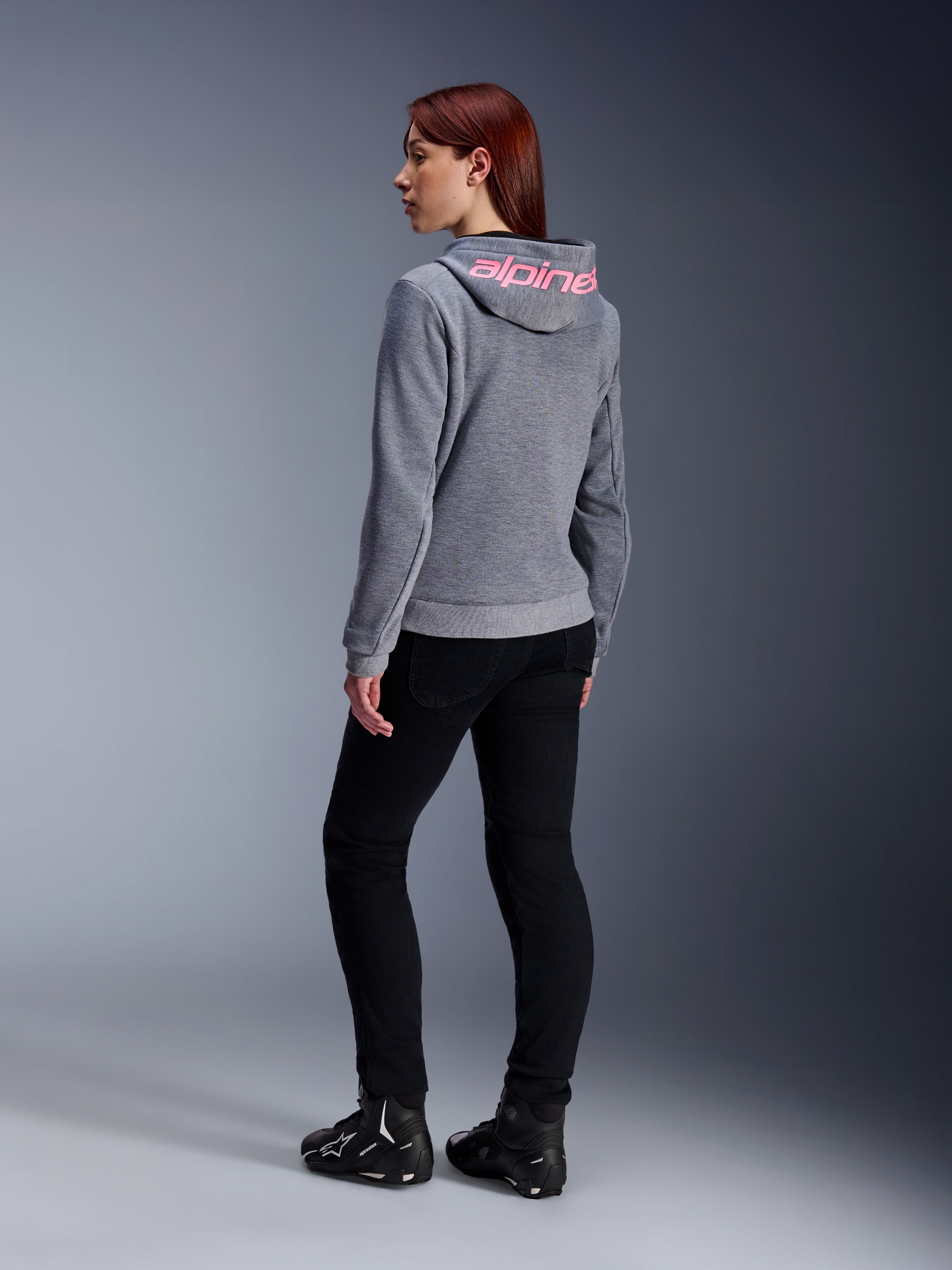 Alpinestars Stella Chrome V2 Sport Hoodie, MC-hoodie för dam, gråmelerad med rosa fluo-logotyp på huvan, vy bakifrån, bärs med svarta byxor och MC-skor, avslappnad urban streetstyle med motorcykelskydd