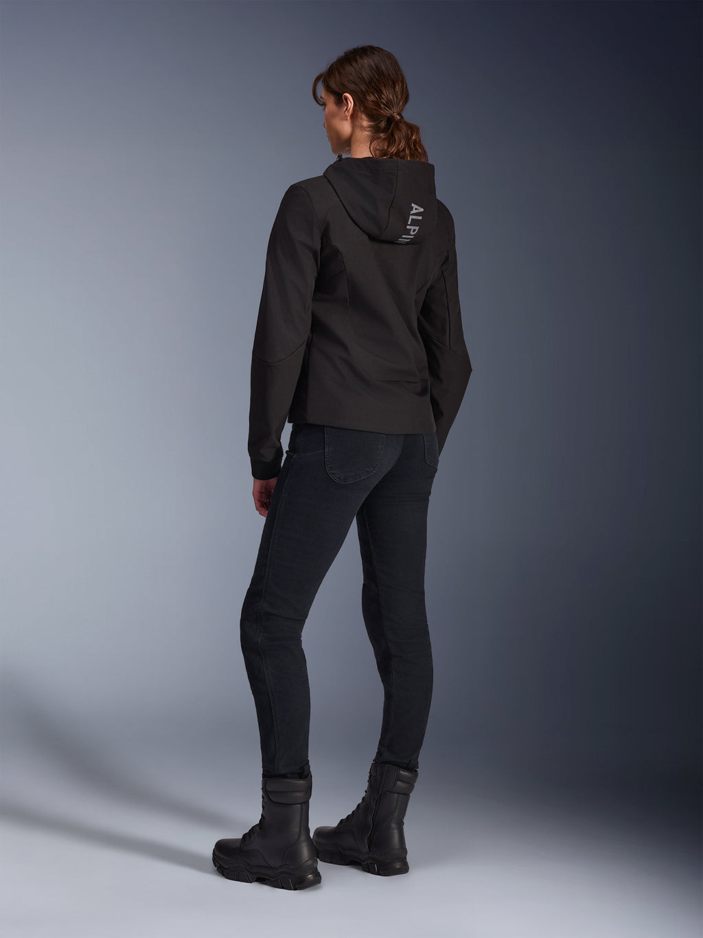 Alpinestars Stella Radium Tech Hoodie, svart urban motorcykelhuvtröja för dam, vy bakifrån som visar 'ALPIN'-logotyp på huvan, matchad med svarta tekniska körbyxor och svarta stövlar, lätt vindtätt tekniskt skal.