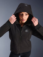 Kvinna som bär Alpinestars Stella Radium Tech Hoodie i svart, urban motorcykelhoodie med huvan uppe, med rund Alpinestars-logotyp på bröstet, ribbade muddar och vindtät 3-lagerskonstruktion
