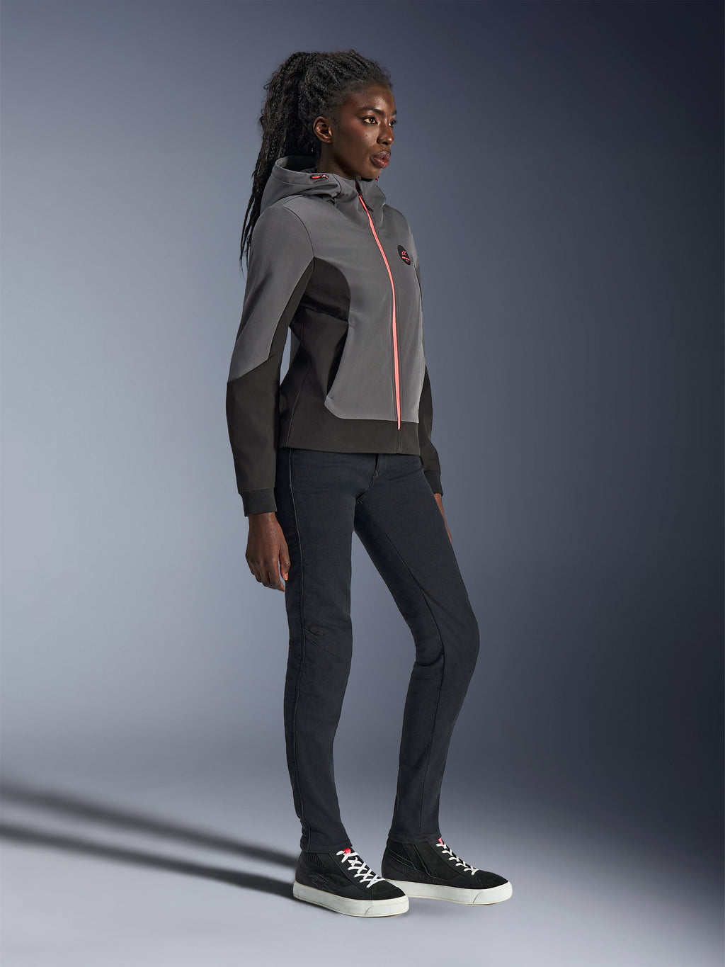 Alpinestars Stella Radium Tech Hoodie, urban mc-hoodie, mörkgrå och svart med stark orange dragkedja, bärs med svarta byxor och svarta sneakers, damspecifik atletisk passform