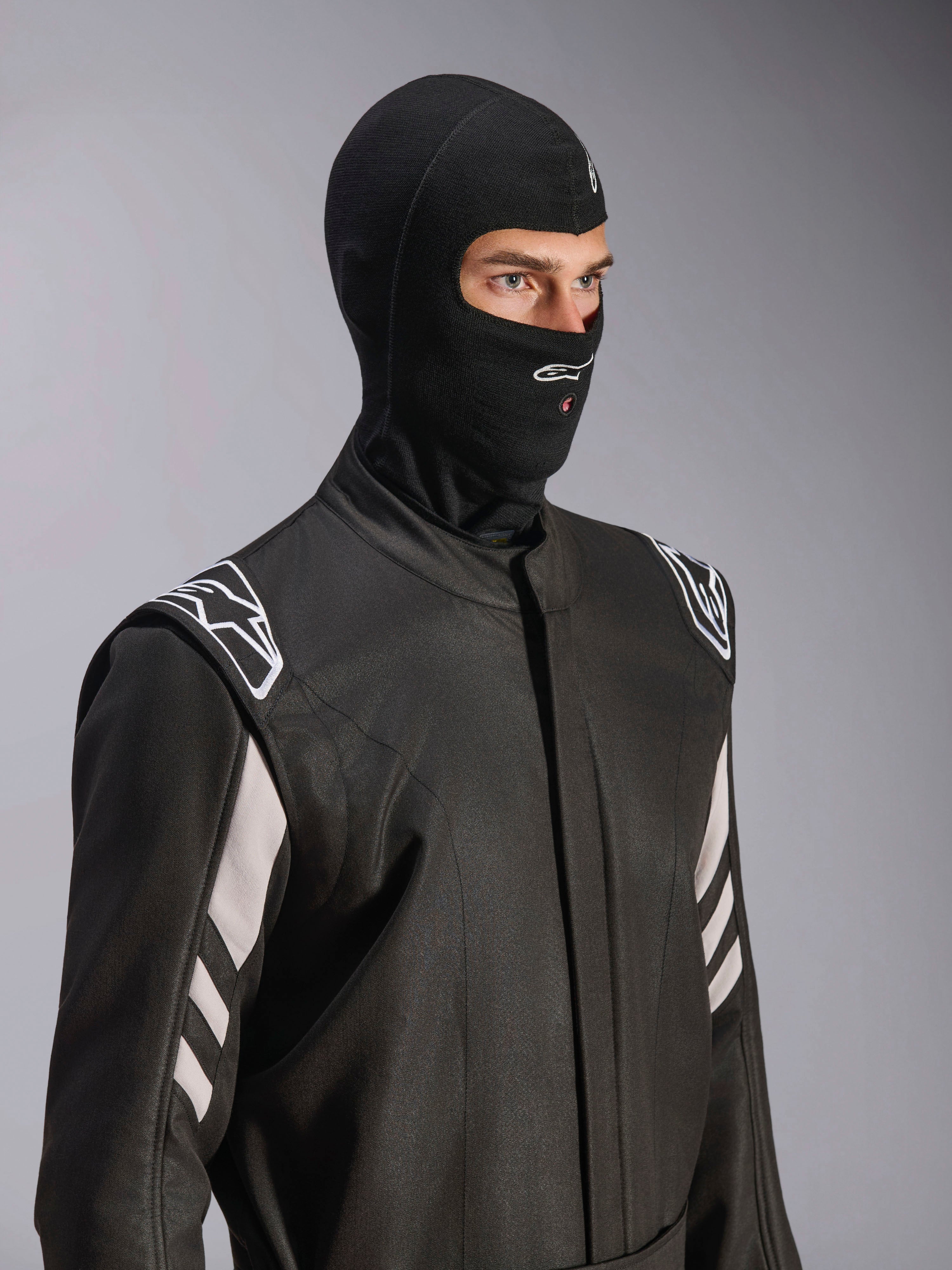 Alpinestars ZX Evo V3 Balaklava, svart, flamsäker huva för bilracing, bärs av en modell i en svart racingoverall med vita detaljer, har Alpinestars-logotyp på hakan, öppning för vätskeslang, professionell skyddsutrustning för motorsport