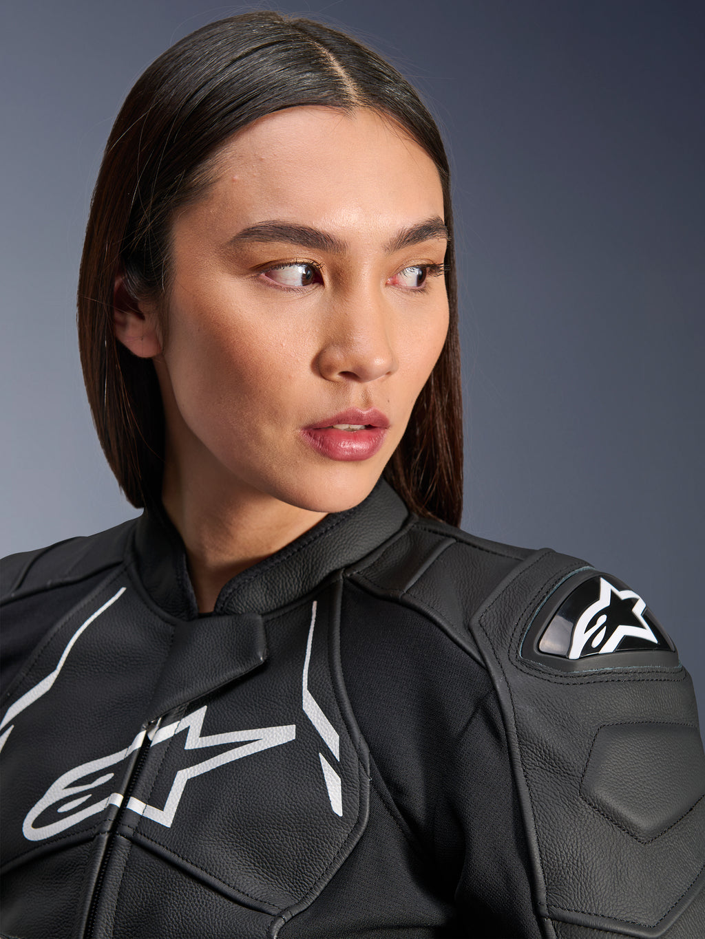 Kvinna som bär Alpinestars Stella Dusk läderjacka i svart och vitt, närbildsporträtt med den vita Alpinestars-logotypen på bröstet och det externa DFS-axelskyddet, premium läderkonstruktion för motorcykelracing på väg