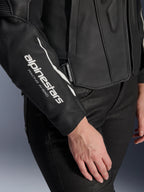 Närbild på Alpinestars Stella Dusk läderjacka, svart motorcykeljacka i läder för dam, med vit 'alpinestars RACING AHEAD'-logotyp på ärmen, premiumtextur i nötläder, buren med svarta byxor