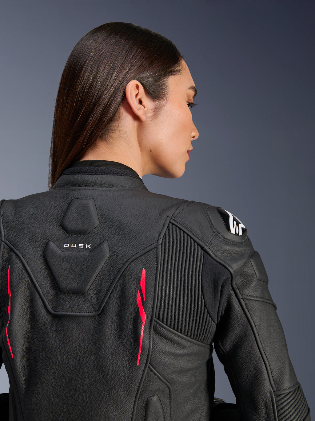 Kvinna som bär Alpinestars Stella Dusk läderjacka, svart läder med Diva Pink-detaljer och vit logotyp på axeln, vy bakifrån som visar DUSK-märkning och dragspelspaneler, sportig ergonomisk design