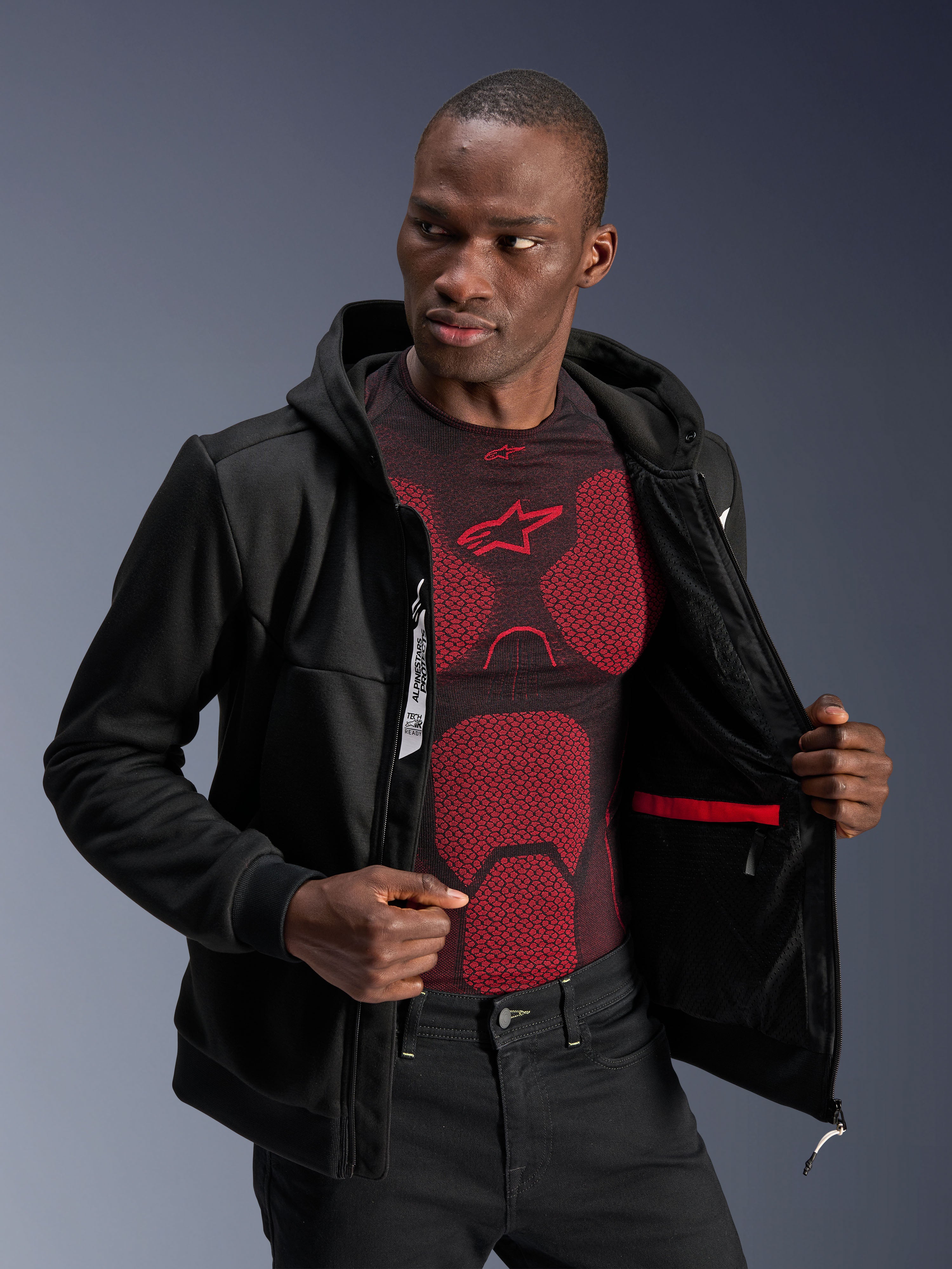 Alpinestars Chrome V2 Sport Hoodie, Black, male model wearing the jacket open to show the interior lining, red waterproof pocket, and internal branding, worn over a red and black base layer, casual urban motorcycle gear