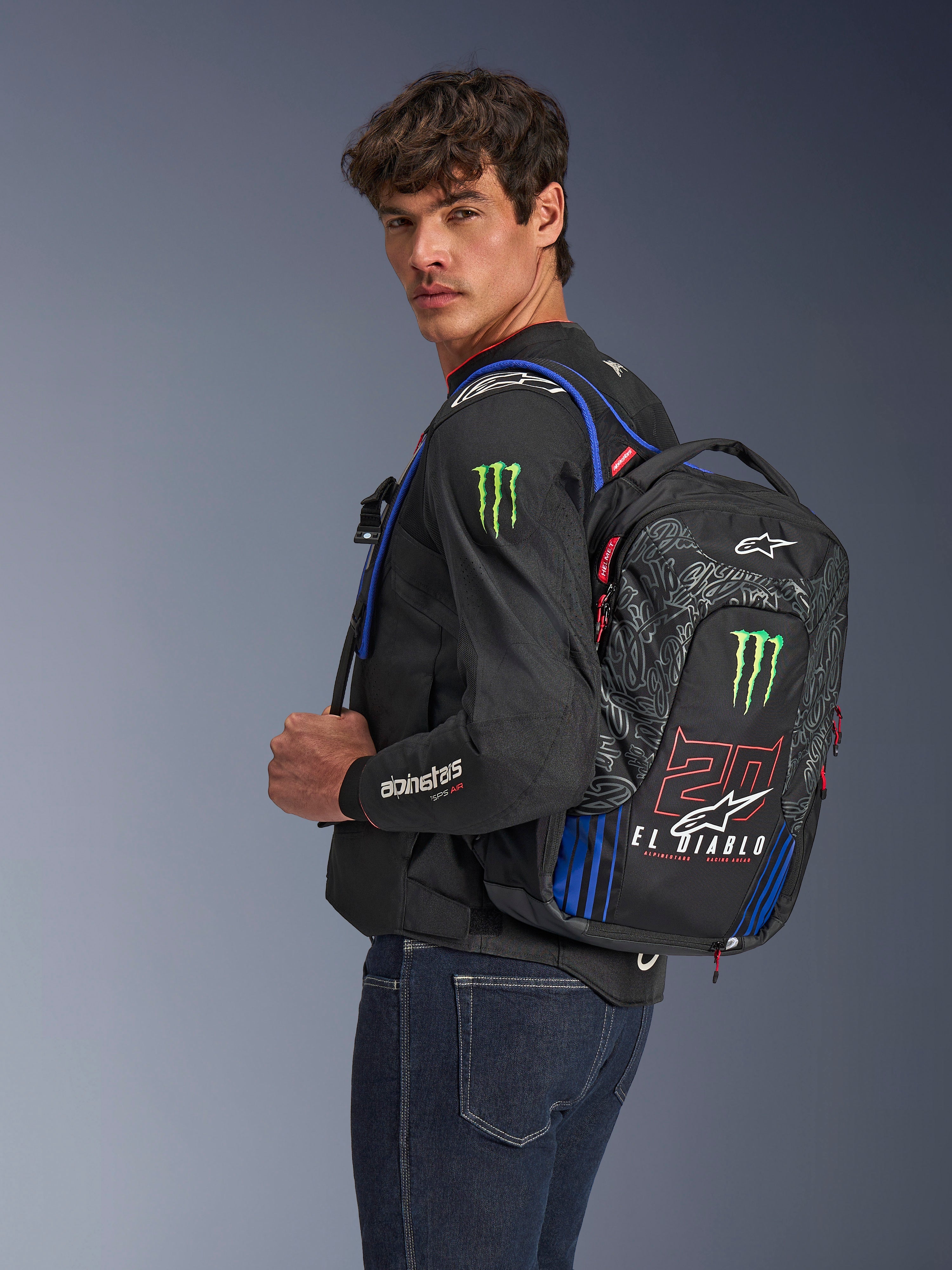 Alpinestars FQ20 City Hunter V2 Monster ryggsäck, motorcykelryggsäck, svart med fluorescerande rött, blått och grönt, med Monster Energy- och Fabio Quartararo 'El Diablo'-logotyper, bärs av en modell med svart motorcykeljacka och jeans, strömlinjeformad design för stadskörare