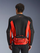 Alpinestars MM93 Waist Bag, röd och svart, buren över en svart och röd motorcykeljacka, med Marc Marquez 93-logotyp, justerbart bälte och fack med dragkedja, funktionell racinginspirerad accessoar