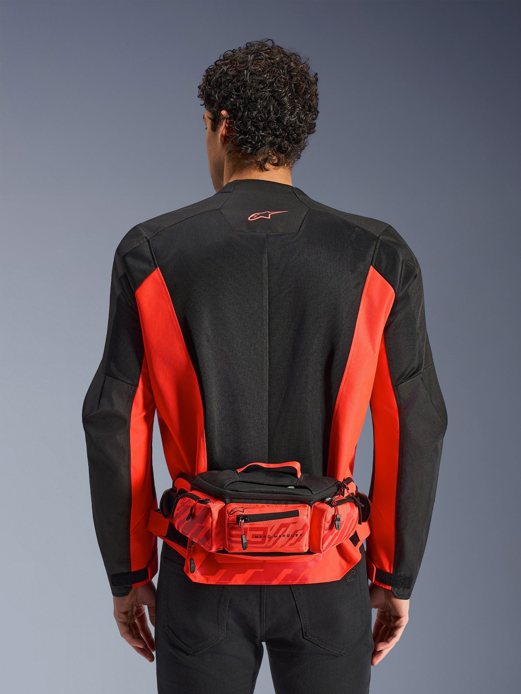 Alpinestars MM93 Waist Bag, Red and Black, worn over a black and red motorcycle jacket, featuring Marc Marquez 93 branding, adjustable belt and zippered compartments, functional racing-inspired accessory