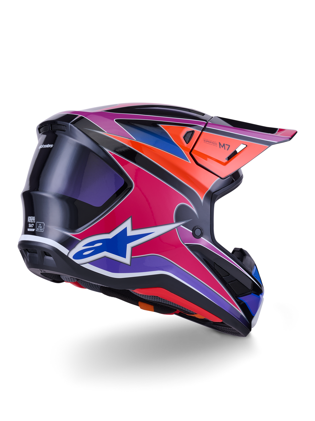 Alpinestars S-M7 Fuse hjälm, motocrosshjälm, glansig finish i blått, lila och rosa med orangea och svarta detaljer, vy snett bakifrån som visar det aerodynamiska skalet, visiret och ventilationsöppningarna, professionellt skydd för off-road-racing