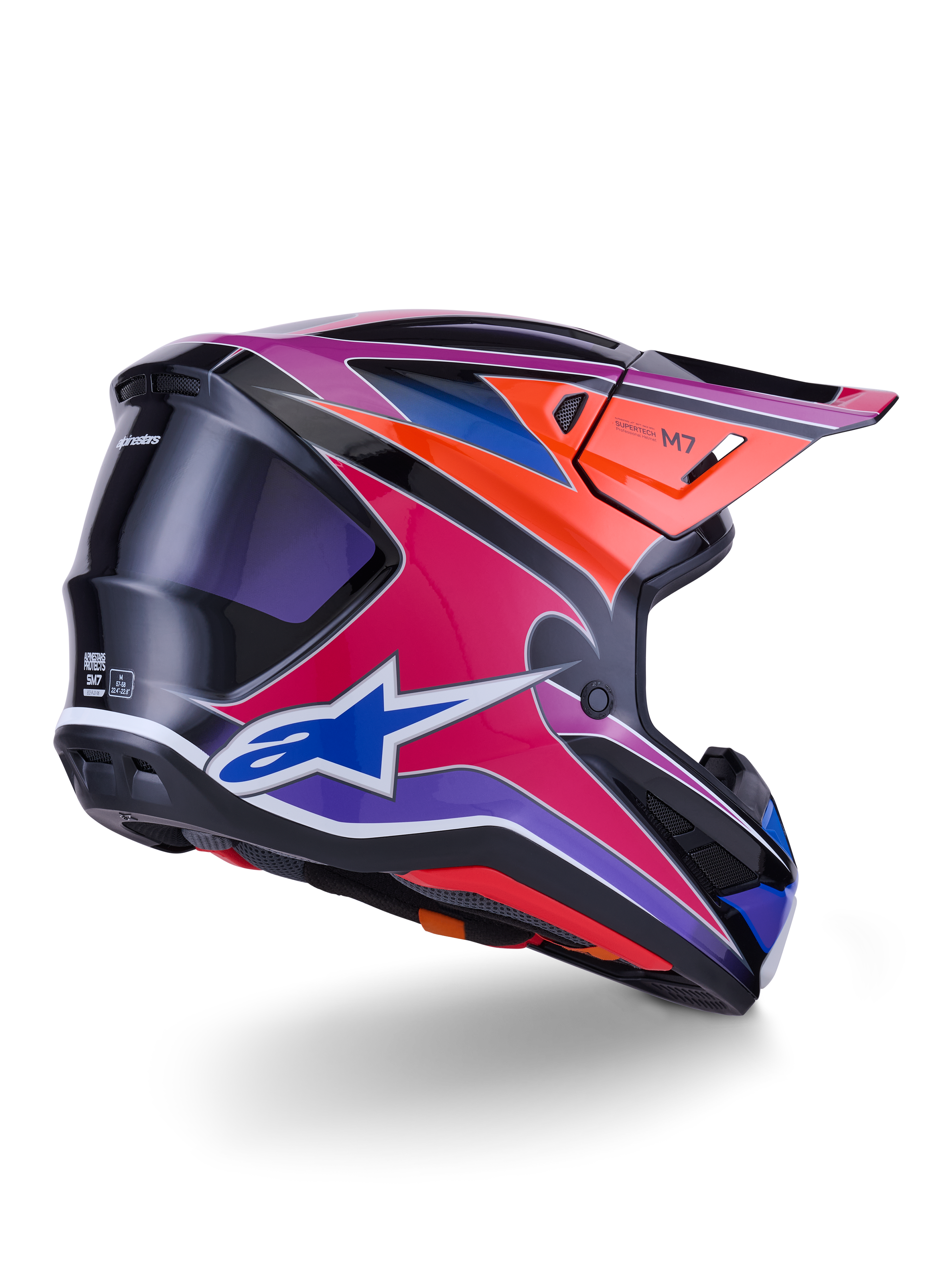 Alpinestars S-M7 Fuse hjälm, motocrosshjälm, glansig finish i blått, lila och rosa med orangea och svarta detaljer, vy snett bakifrån som visar det aerodynamiska skalet, visiret och ventilationsöppningarna, professionellt skydd för off-road-racing