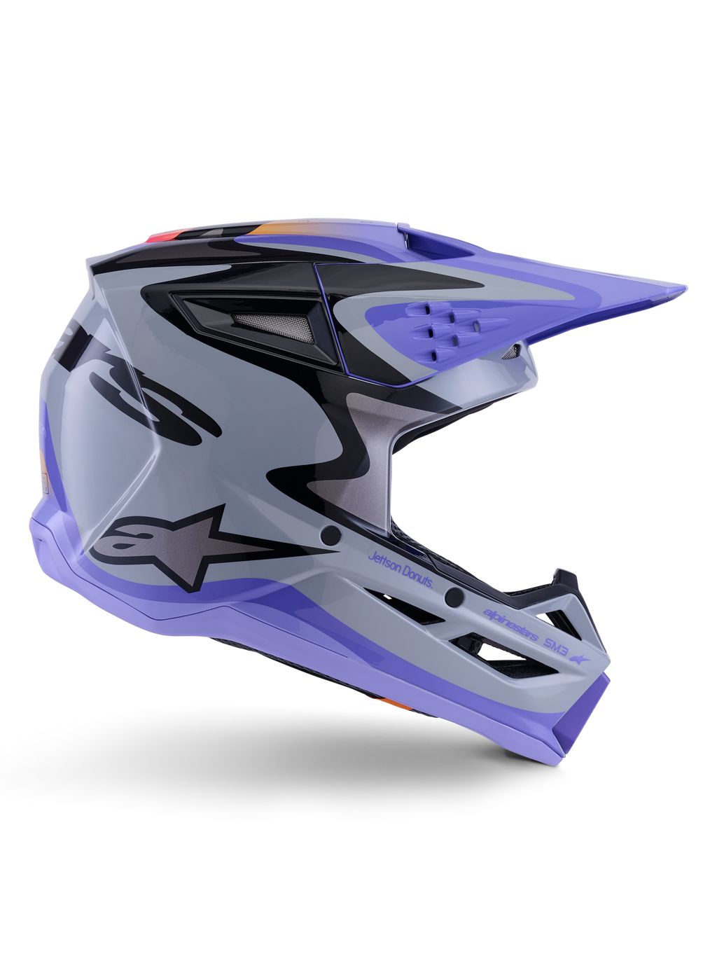 Alpinestars S-M3 Jettson-hjälm ECE 22.06, motocrosshjälm, grå, lila och svart glansig, sidoprofil med lila visir och hakskydd, aerodynamiskt skal med svart grafik, flera ventilationsöppningar och "Jettson Donuts"-logotyp på sidan.