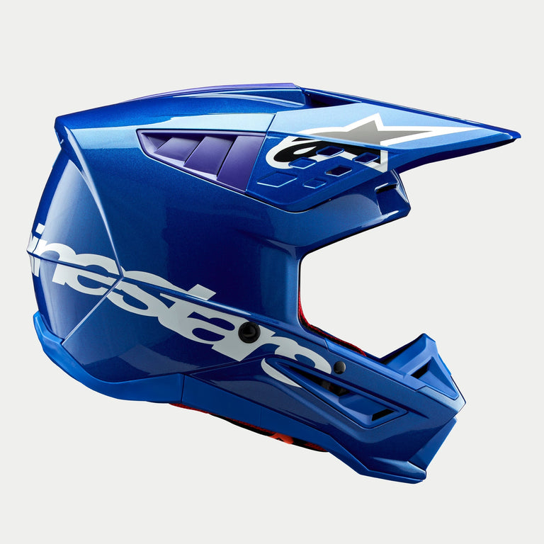 Alpinestars S-M5 Corp Helmet ECE, Blue Glossy motocross helmet, side profile view, bold white Alpinestars branding across the side, purple accents in ventilation ports, lightweight aerodynamic shell for off-road performance