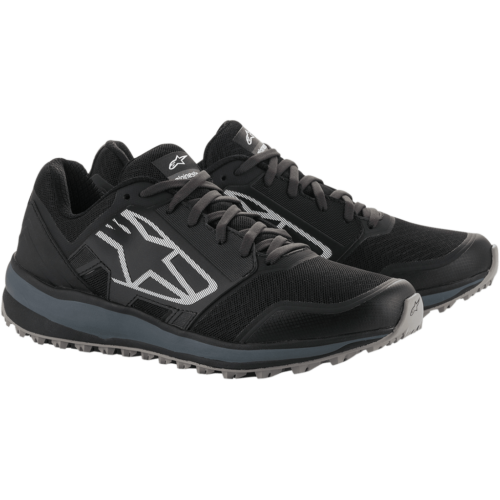 Alpinestars Meta Trail-skor, prestationslöparskor, svarta och mörkgrå, stor vitrandig Astars-logotyp på sidan, snörning med en robust grå sula, designade för heldagskomfort i paddocken