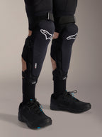 Alpinestars A-Impact Plasma Pro Knee Shin Protectors, Black and White, featuring the white Alpinestars logo and triple strap closure system, worn with black socks and black athletic shoes, durable off-road cycling protection
