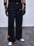 Alpinestars RSRV Arena Suit Pants, svarta racingbyxor med McLaren-logotyp, orangea detaljer på sidan och knä, person iklädd med svarta och orangea handskar samt vita racingskor