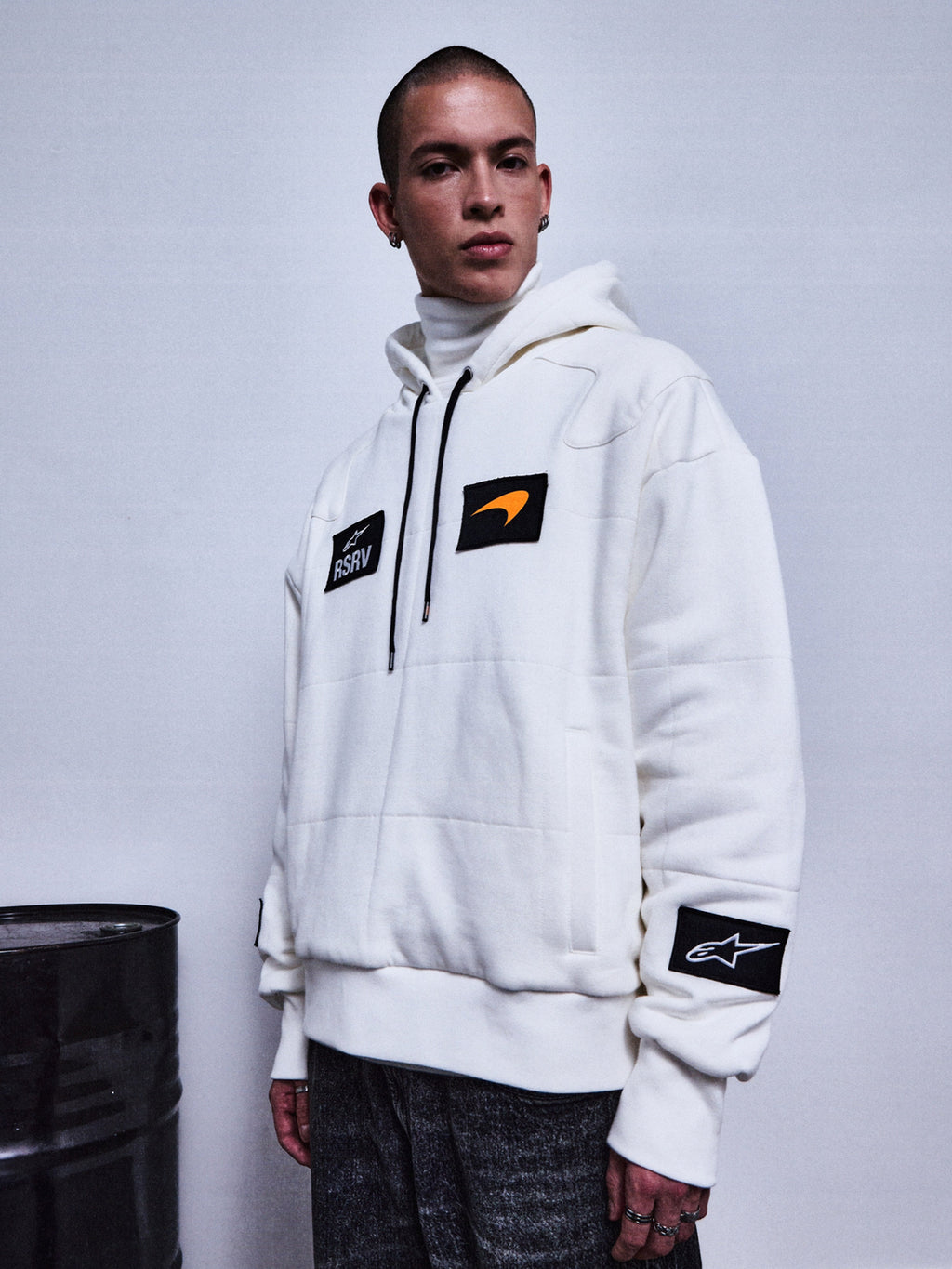 Alpinestars RSRV Rival Hoodie, vit premium streetwear-hoodie med svarta patches, orange swoosh-detalj och RSRV-logotyp, unisex lyxkollektion, person iklädd hoodie med polotröja