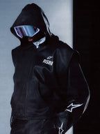 Alpinestars RSRV Axis läderhuvtröja, svart premium läderjacka med huva, futuristiska reflekterande skyddsglasögon, vita stjärndesigner på ärmarna, dragkedja, slät läderstruktur, modern streetwear-stil