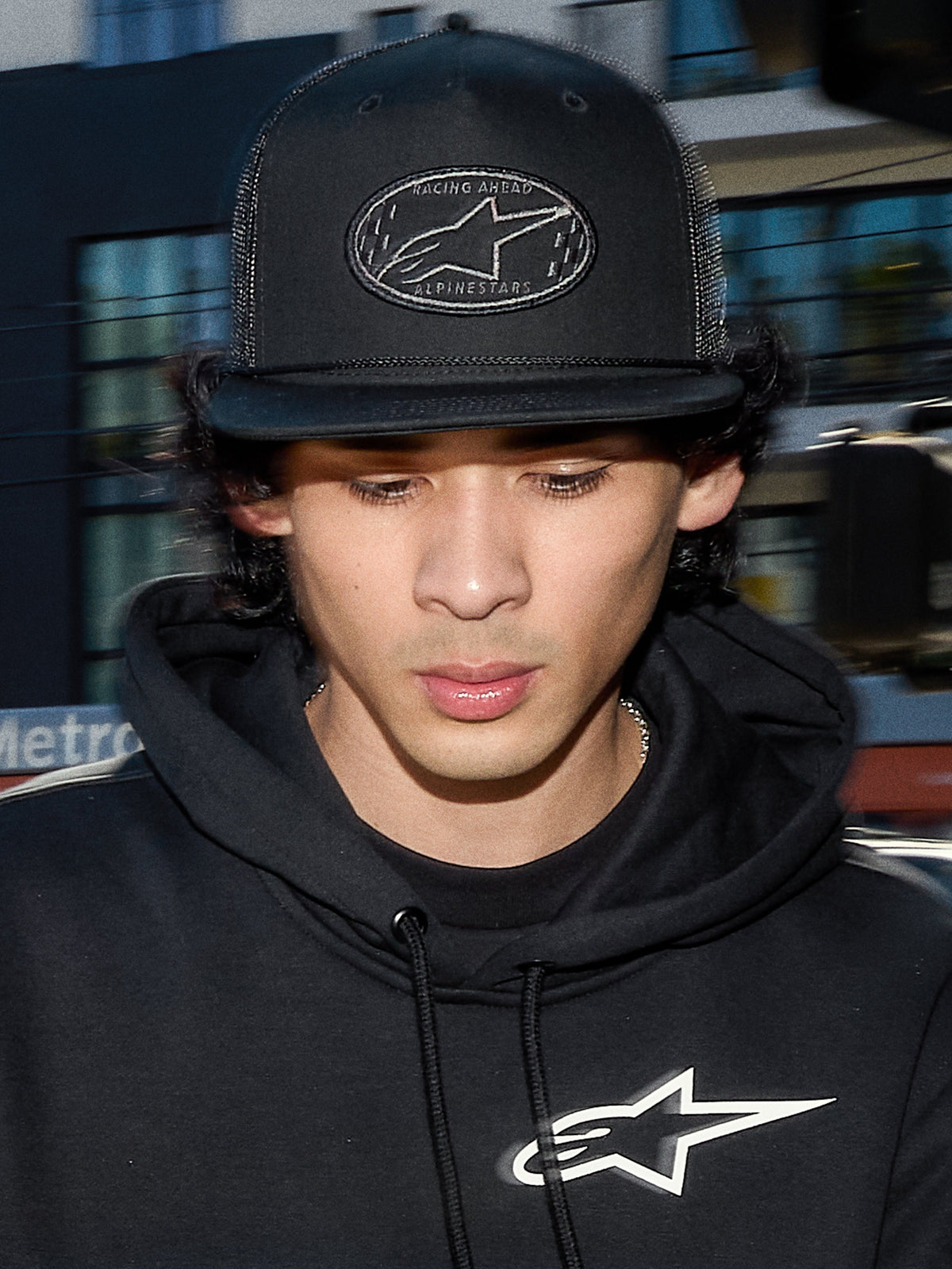 Alpinestars Contender Trucker Hat, svart lifestyle-keps med mesh-baksida, strukturerad krona med ett broderat Astars-logopatch, bärs av en man i en svart Alpinestars-hoodie, avslappnad motorsport-inspirerad streetwear.