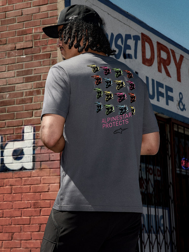 Alpinestars Pop Helmet CSF Tee, kortärmad t-shirt, koksgrå, rygggrafik med färgglada M10-hjälmar och rosa 'ALPINESTAR PROTECTS'-text, avslappnad motorsport-inspirerad streetwear