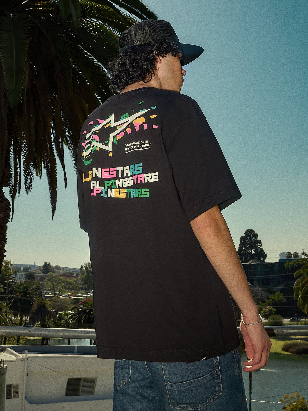 Alpinestars Wild Oversized CSF Tee, kortärmad t-shirt, svart, livfull flerfärgad Astars-logotyp på ryggen, oversized passform, streetwear-livsstilsbild med palmer