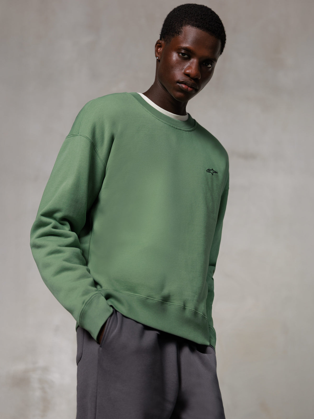 Alpinestars Essentials Ageless Crew, crewneck-tröja, kaktusgrön, med en liten svart Alpinestars-logotyp på bröstet, bärs av en modell med grå byxor, casual lifestyle-streetwear