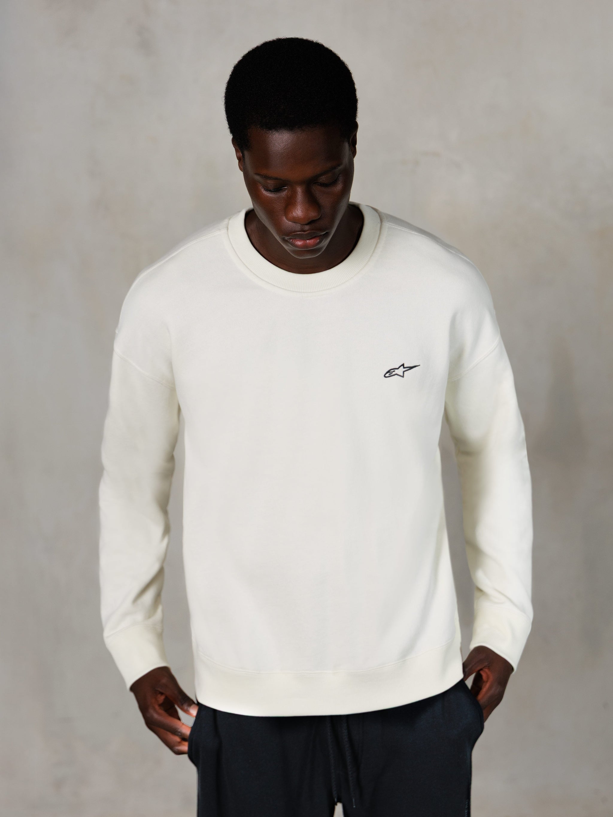 Alpinestars Essentials Ageless Crew, sweatshirt med rund halsringning, Off White, liten svart Alpinestars-logotyp på bröstet, bärs av modell, vardaglig streetwear, mjuk premiumfleece