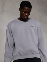 Alpinestars Essentials Ageless Crew, silverfärgad premium crewneck-tröja, med en liten svart Alpinestars-logotyp på bröstet, bärs av en modell, avslappnad lifestyle-streetwear med en mjuk fleecestruktur.