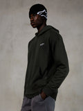 Alpinestars Essentials Ageless Hoodie, Off Black, manlig modell i ledig streetwear, mörk koksgrå stentvättad fleece med en liten vit stjärnlogotyp, matchad med en svart Alpinestars-mössa och gråa byxor