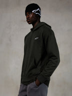 Alpinestars Essentials Ageless Hoodie, Off Black, manlig modell i ledig streetwear, mörk koksgrå stentvättad fleece med en liten vit stjärnlogotyp, matchad med en svart Alpinestars-mössa och gråa byxor