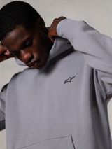 Alpinestars Essentials Ageless Hoodie, Silver, närbild på en man som justerar huvan på den grå huvtröjan, liten svart Alpinestars-logotyp på bröstet, premium motorsportinspirerade vardagskläder